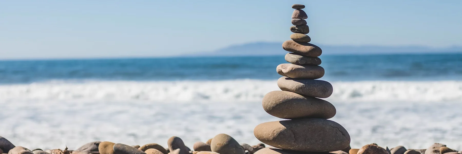 A cairn of balanced stones on a beach with ocean behind it