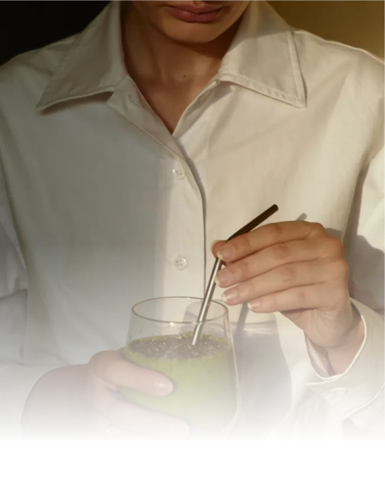 Person in a white shirt holding a green smoothie with a metal straw