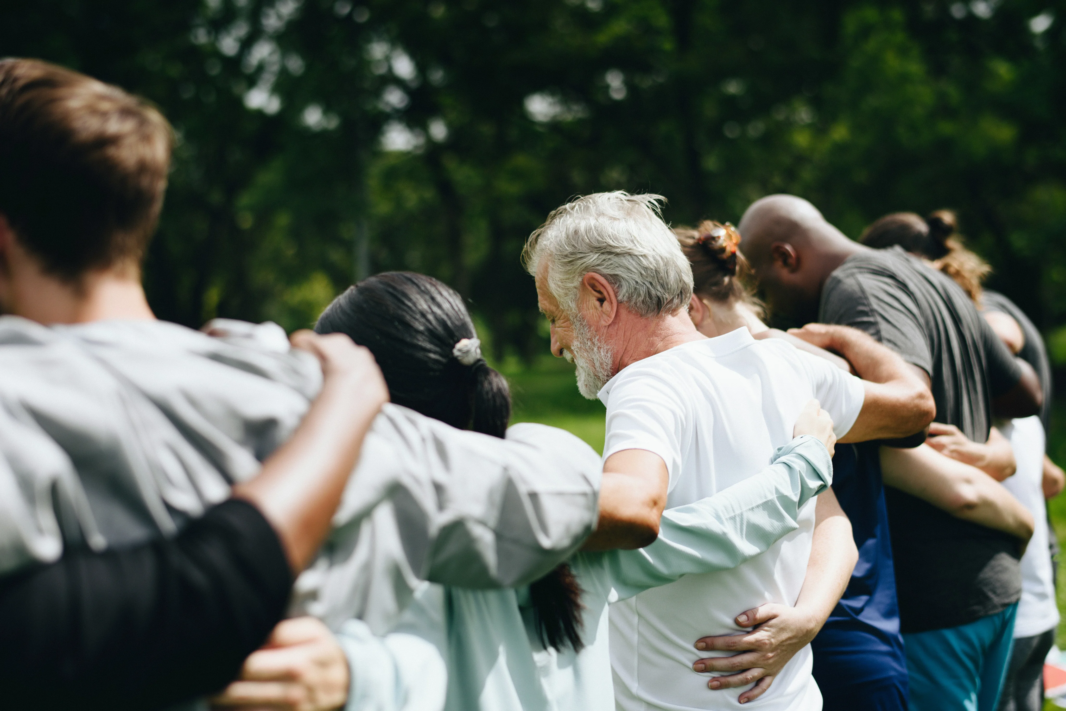 Group of people standing in a circle with arms around each other outdoors