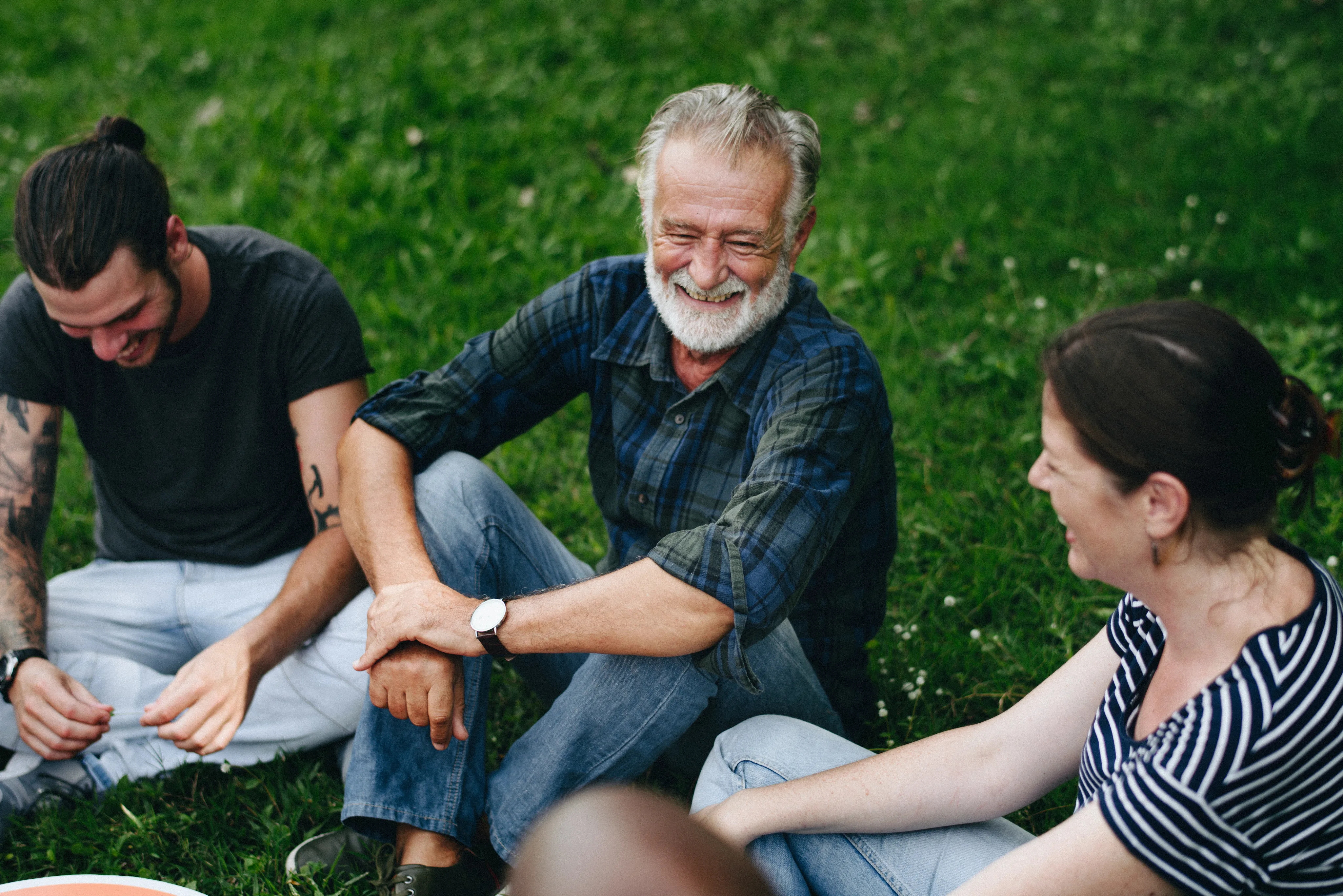 Three people laughing and sitting together on grass in the sunshine